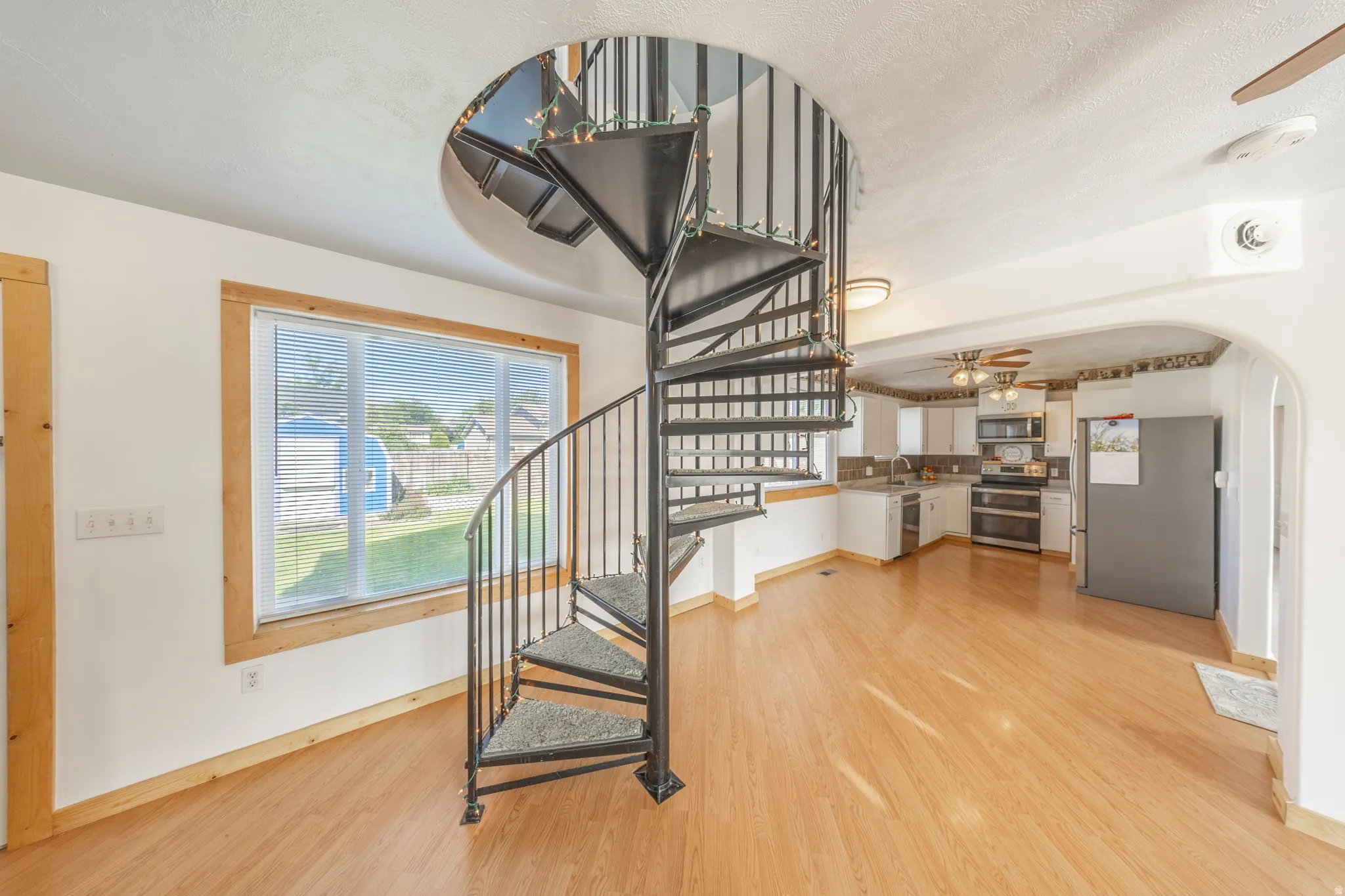 Spiral staircase with carpeted treads, wood-finish flooring, white walls, and a large window