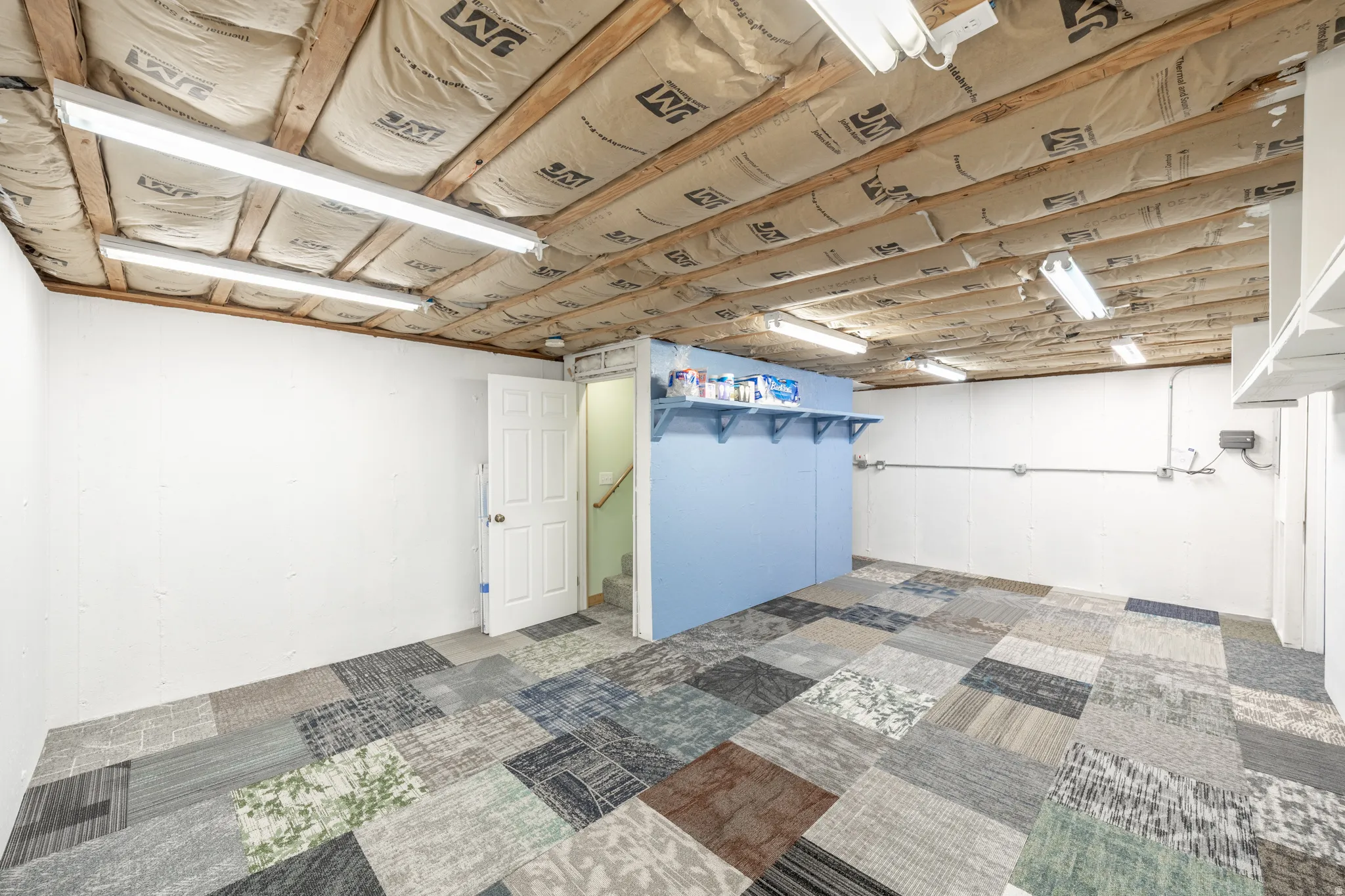 Versatile interior space featuring mixed-pattern flooring, exposed ceiling joists with insulation, and built-in shelving