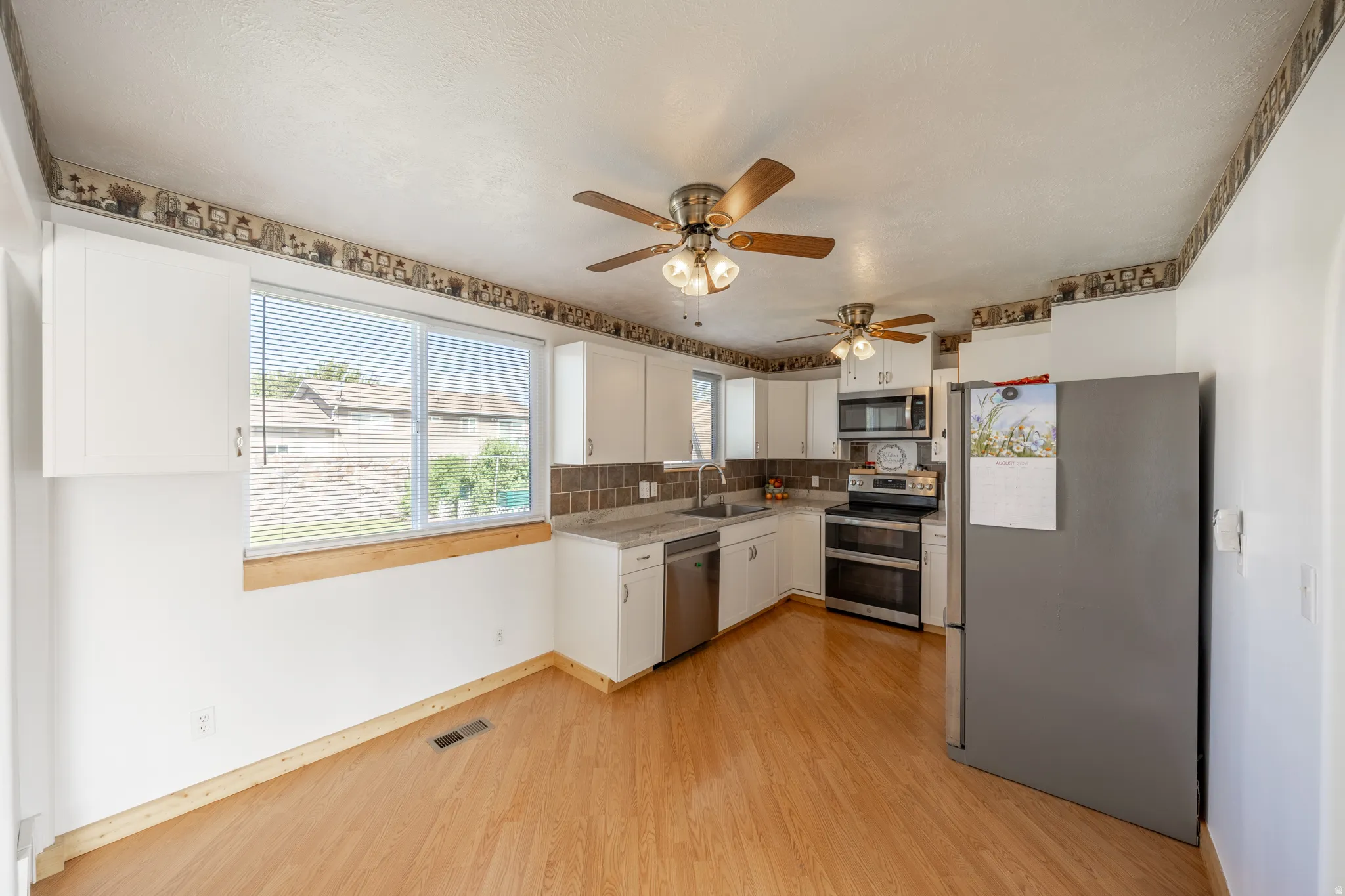 Kitchen featuring wood-finish flooring, white cabinetry, integrated stainless steel dishwasher, and a stainless steel oven/range