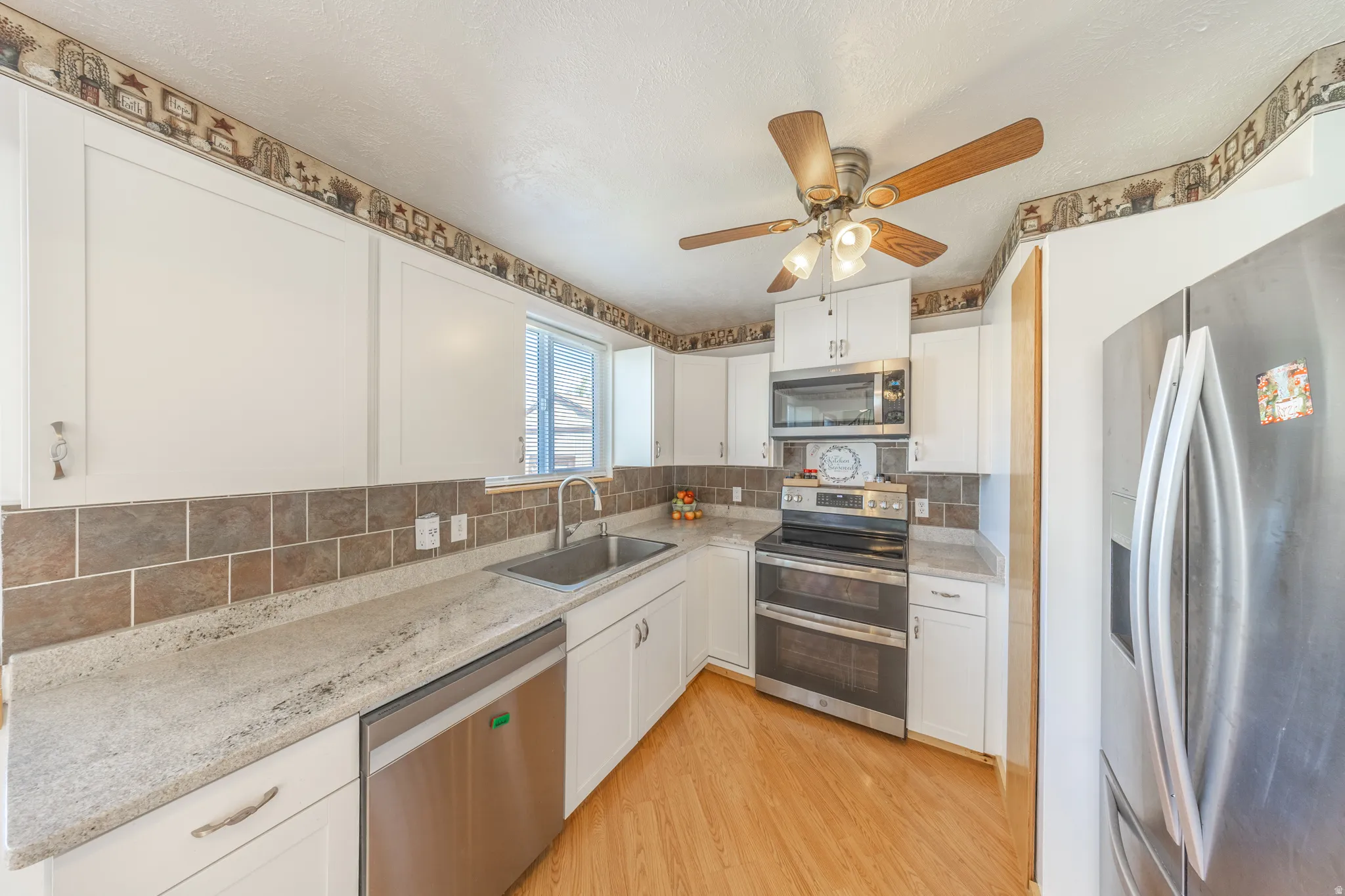 White cabinetry, light-toned countertops, stainless steel appliances, tile backsplash, and wood-finish flooring