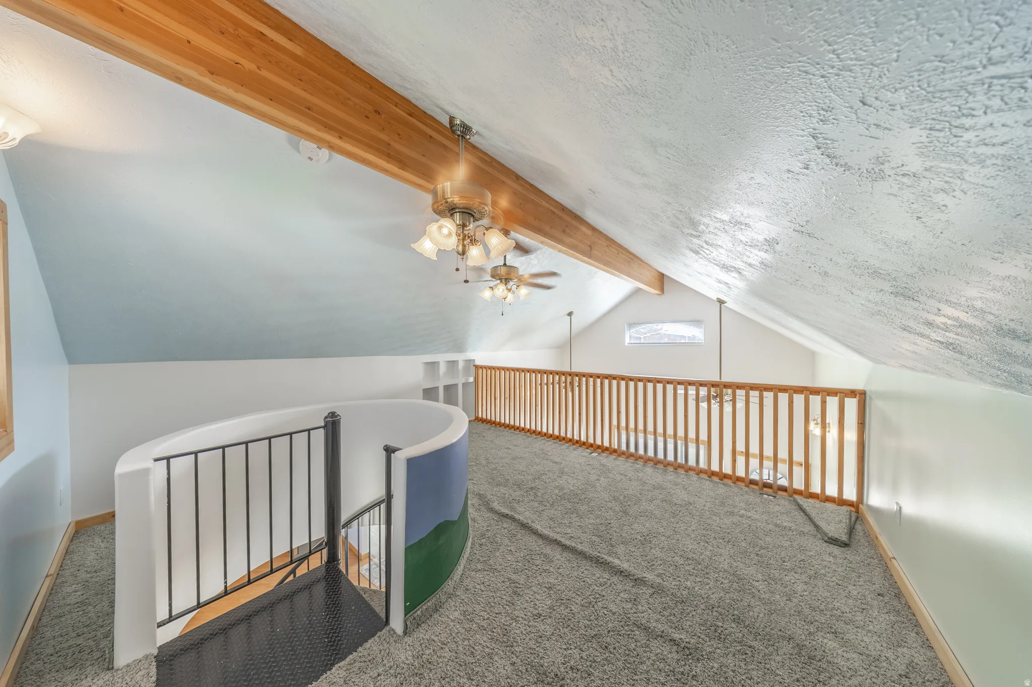 Loft area featuring a spiral staircase with metal railing, wood ceiling beam, two ceiling fans with light kits, and a wood railing overlooking the space below