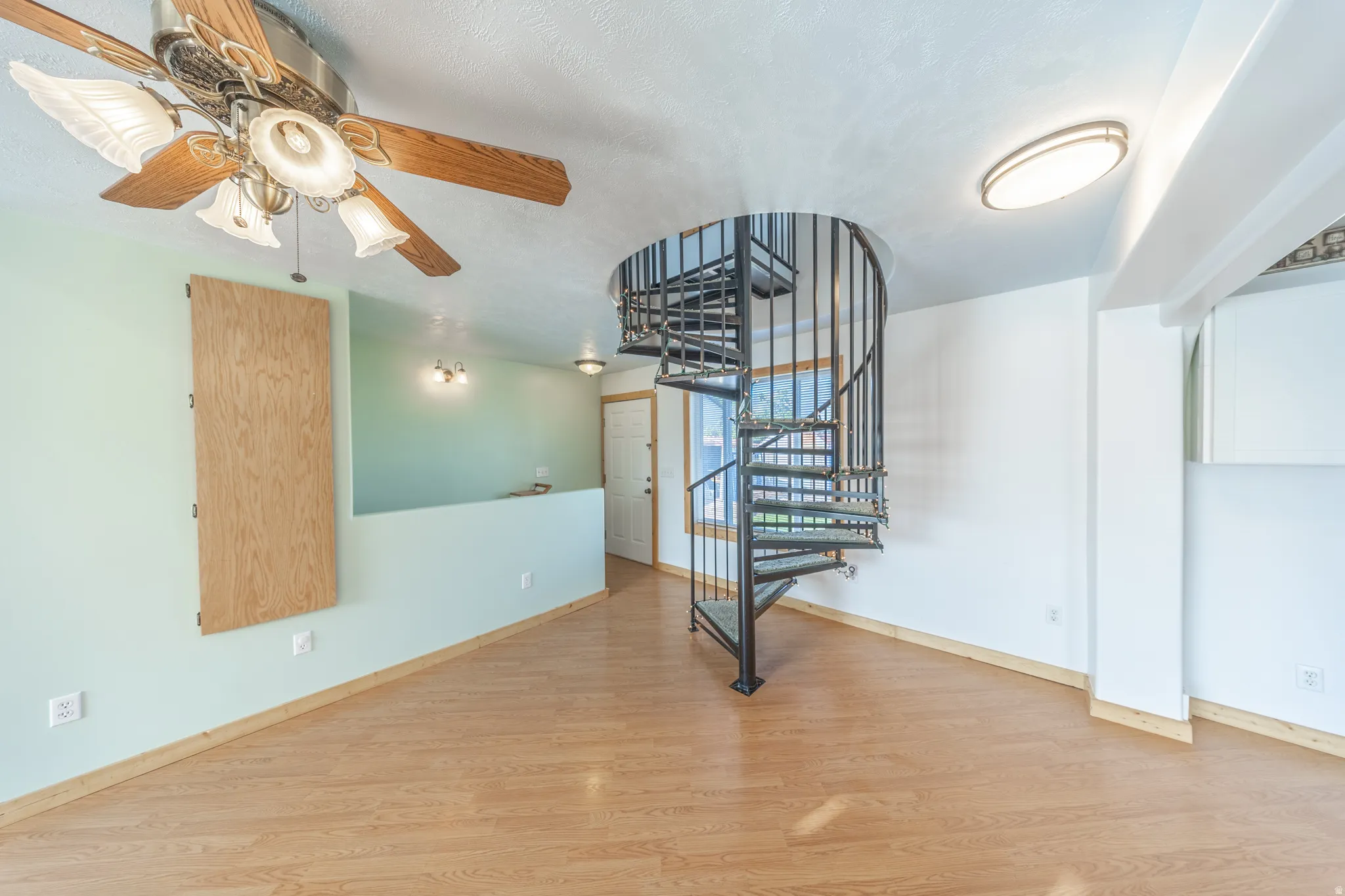 Wood-finish flooring, a spiral staircase, and ceiling fan with integrated lighting