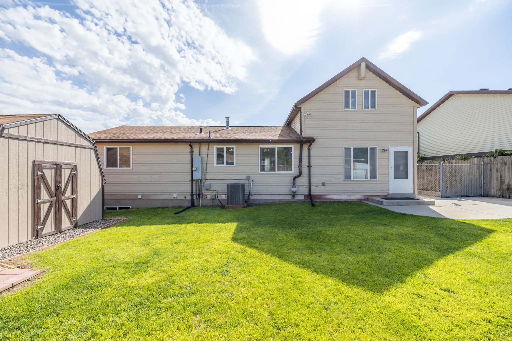 Expansive green lawn, detached storage shed, exterior siding, concrete patio, and a privacy fence