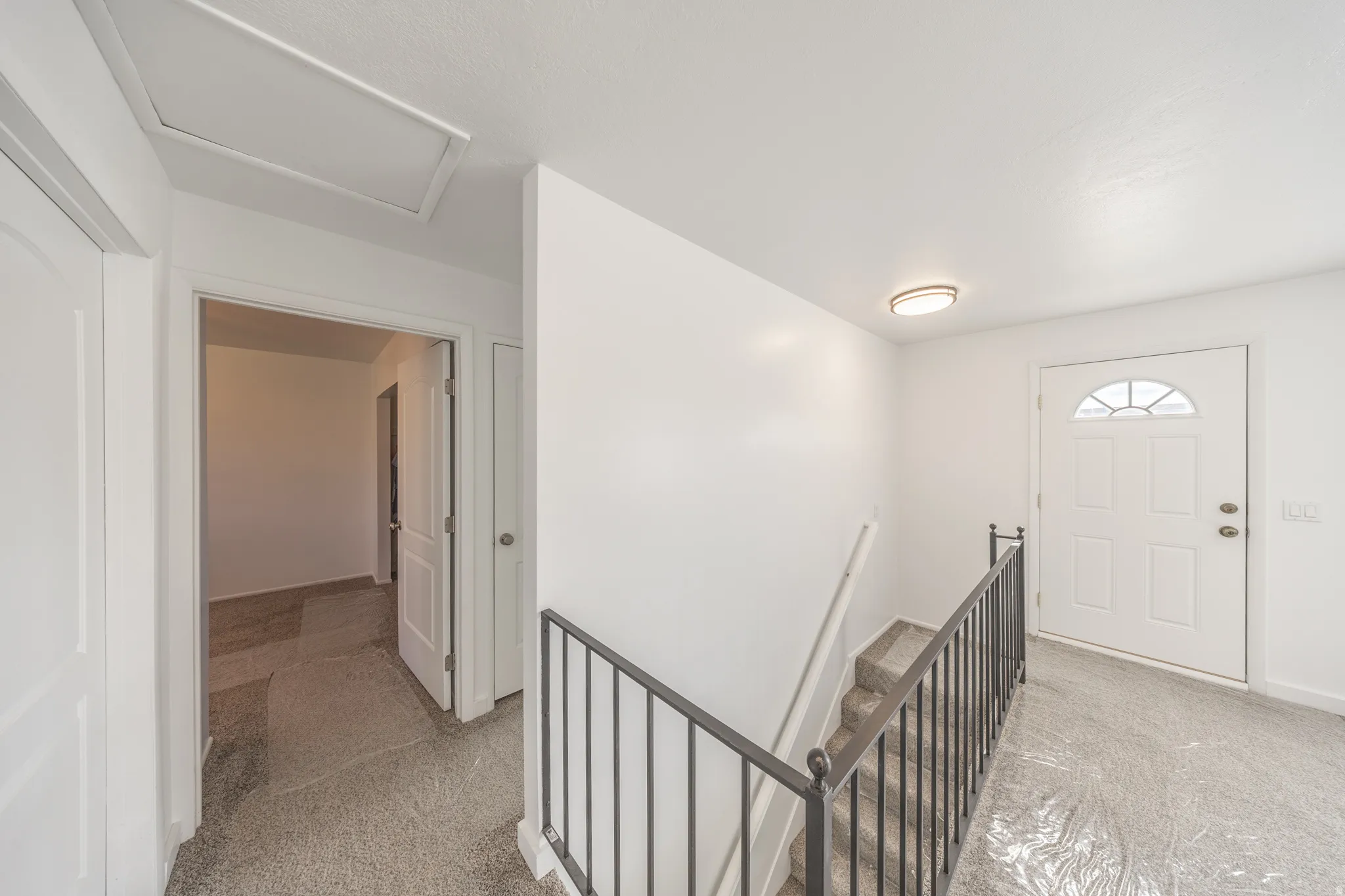 White entryway door with an arched window insert, metal stair railing, and a flush mount ceiling light