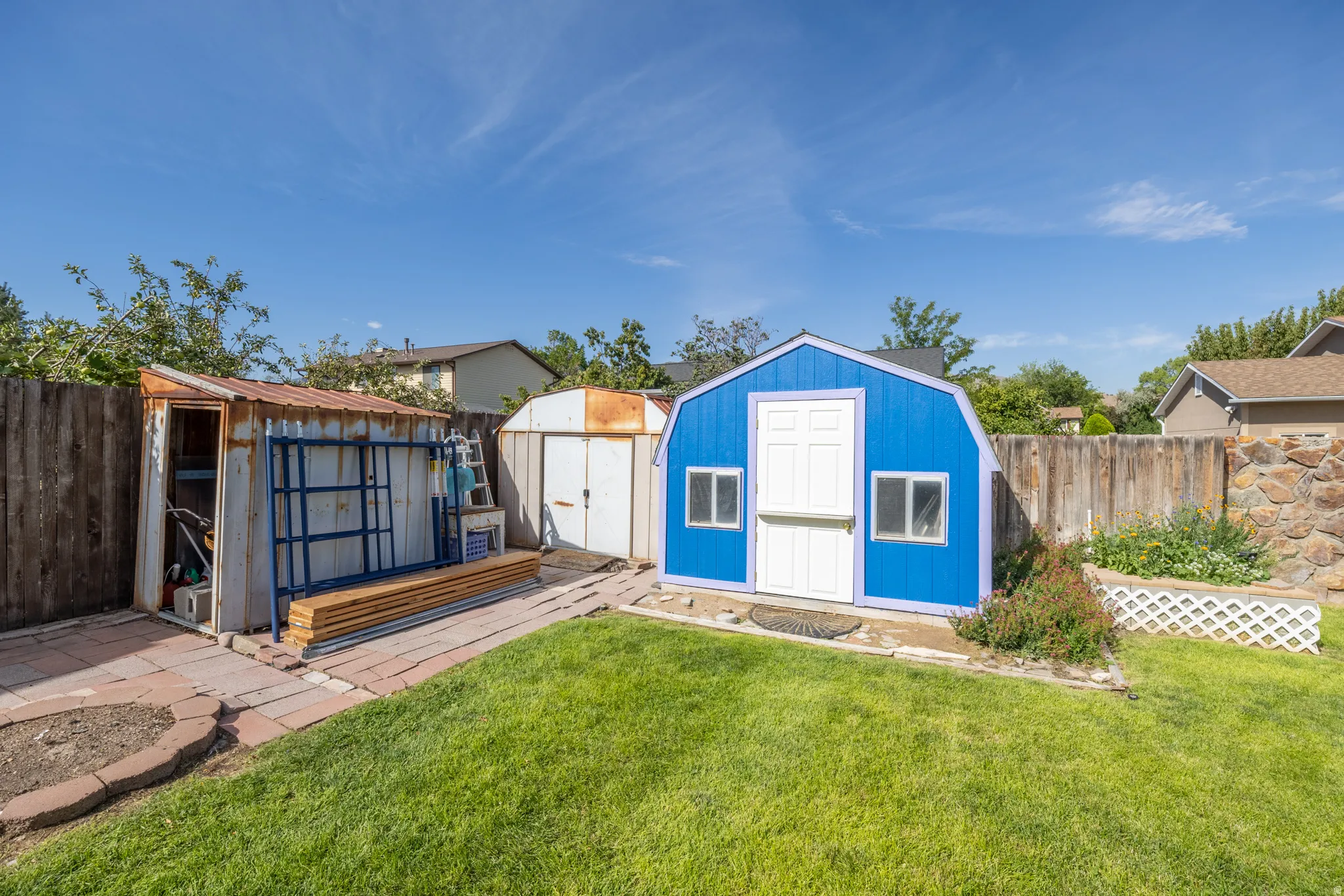 Expansive backyard featuring a manicured lawn, wood fencing, and multiple storage sheds