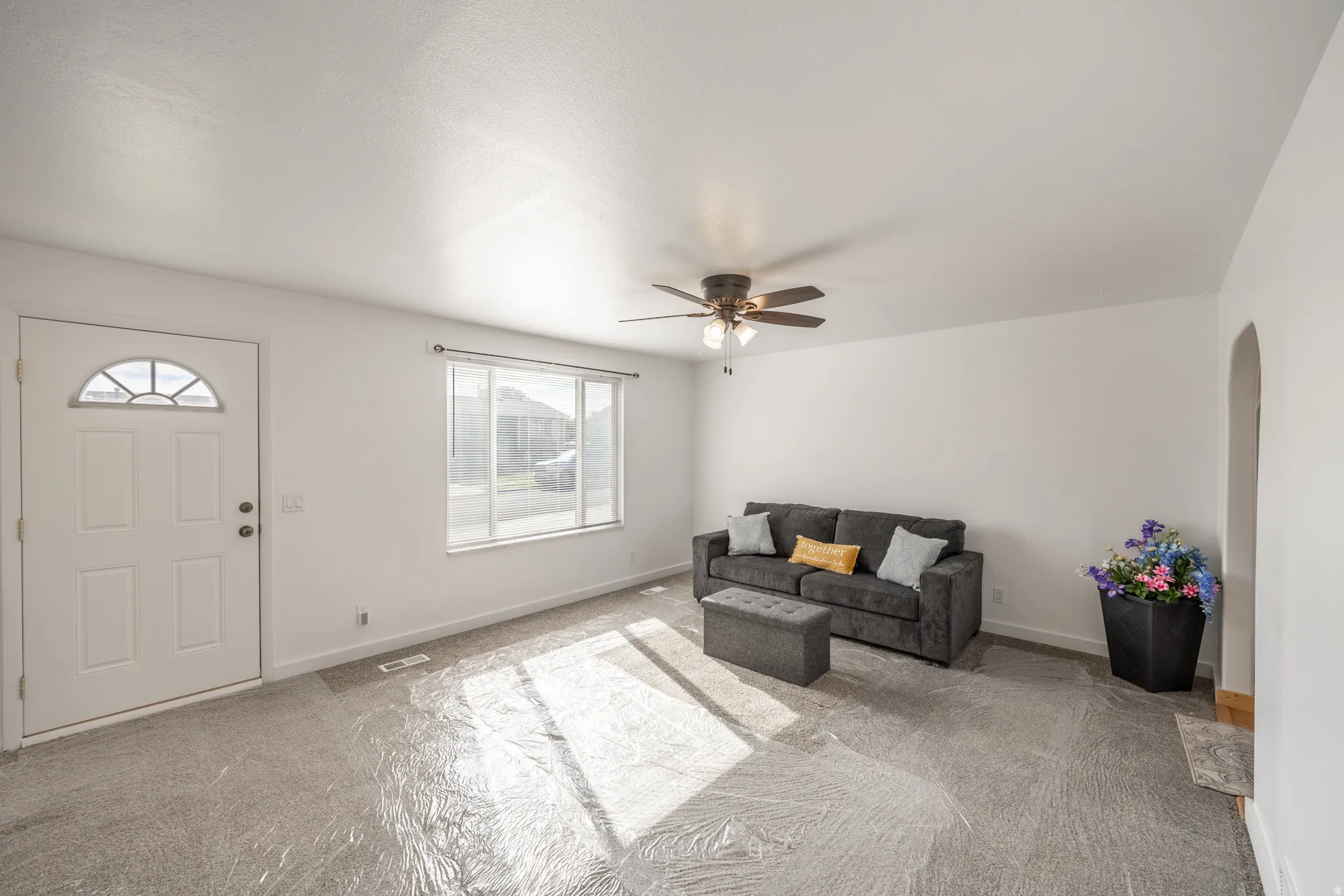 White painted walls, light-toned carpet, ceiling fan, arched doorway, and a window with blinds