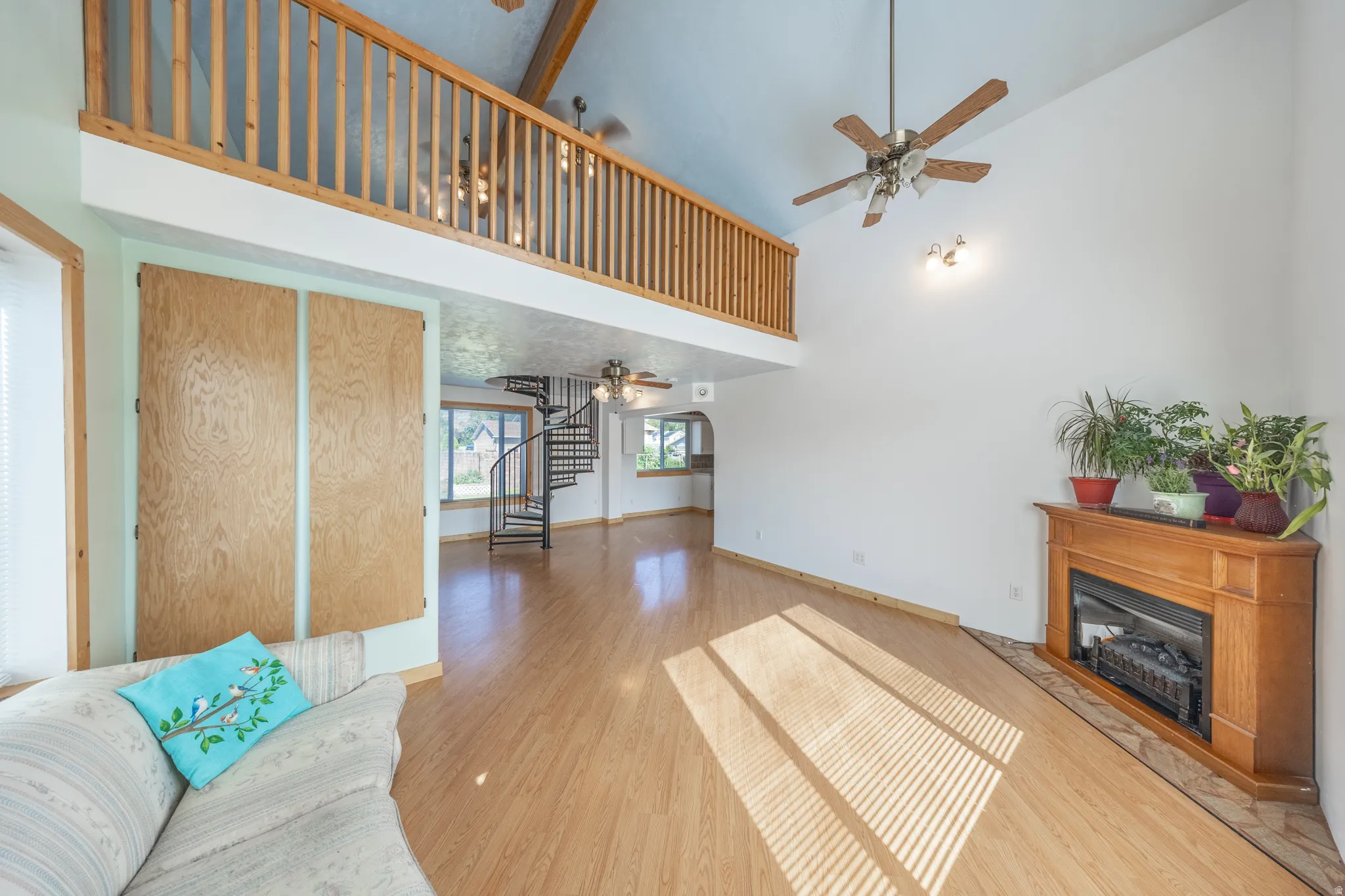 Vaulted ceiling with exposed wood beams, wood-finish flooring, corner fireplace with wood mantel, and a spiral staircase