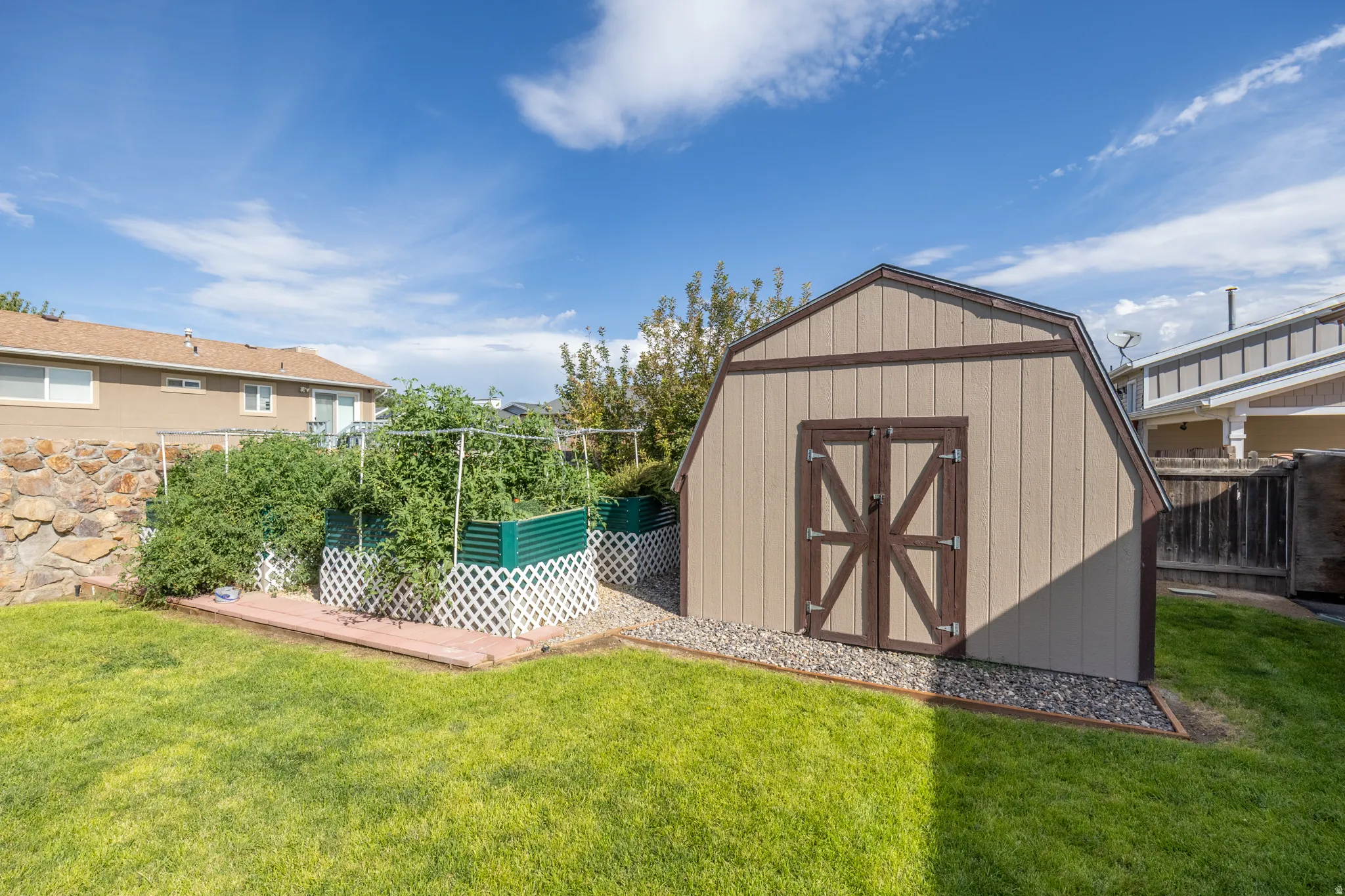 Storage shed with double doors, established raised garden beds, decorative lattice, and a stone retaining wall