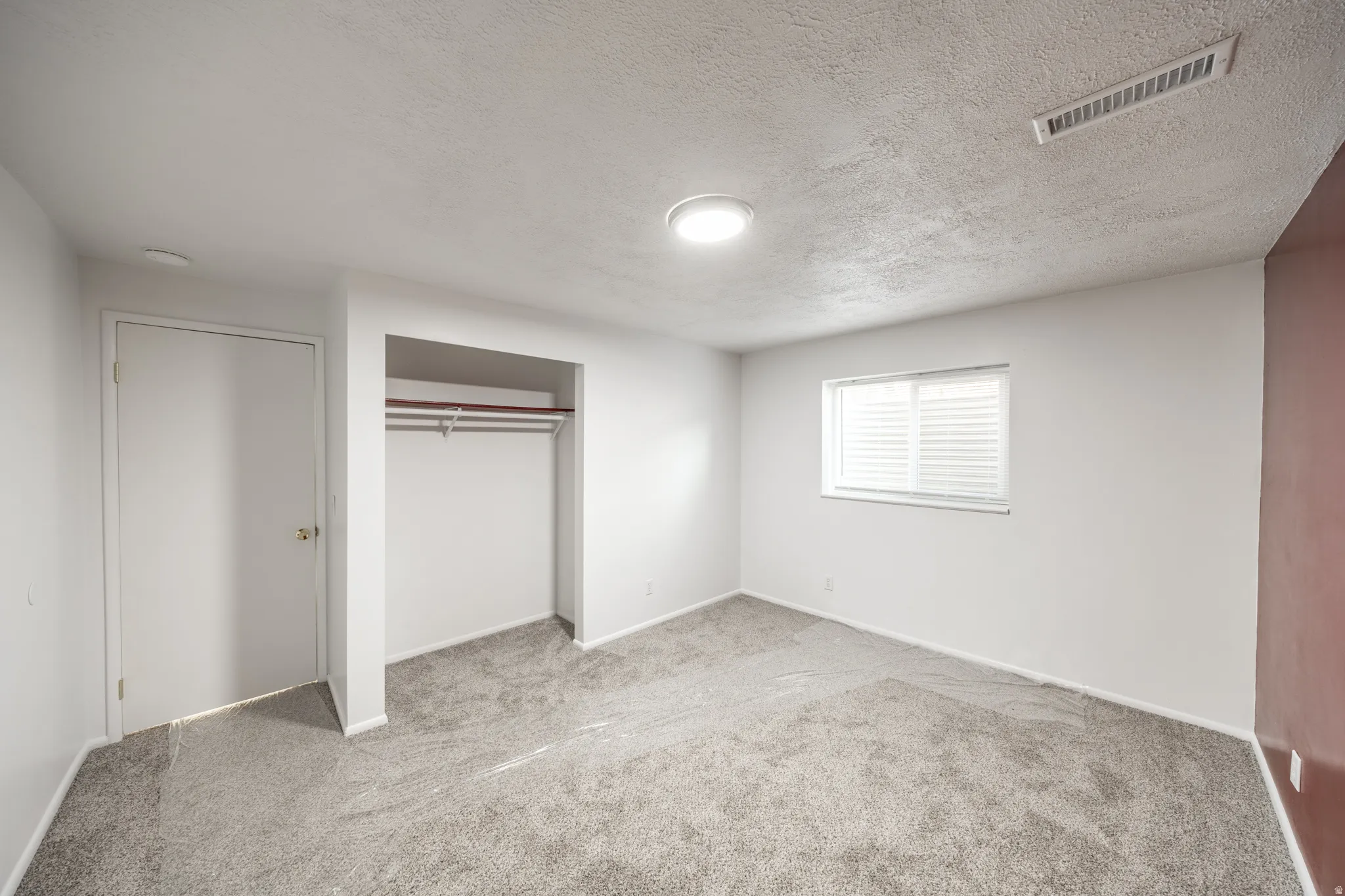Neutral wall paint with an accent wall, window with blinds, and built-in closet with hanging rod