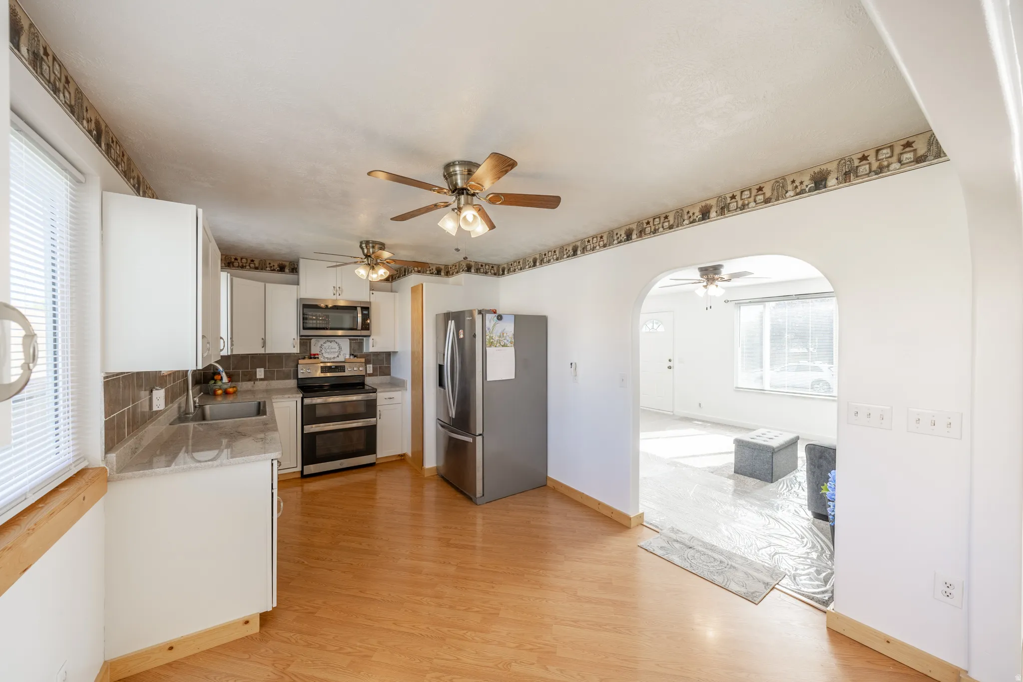 Kitchen featuring wood-finish flooring, stainless steel appliances, white cabinetry, brown tile backsplash, and light-toned countertops