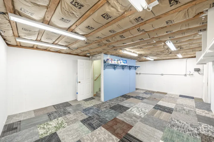 Versatile interior space featuring mixed-pattern flooring, exposed ceiling joists with insulation, and built-in shelving