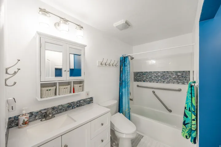 White vanity with integrated sink, mosaic tile backsplash, and mirrored medicine cabinet