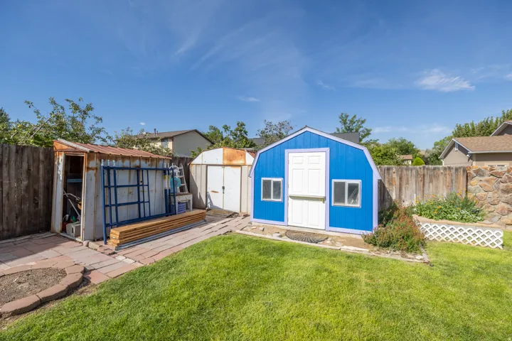Expansive backyard featuring a manicured lawn, wood fencing, and multiple storage sheds