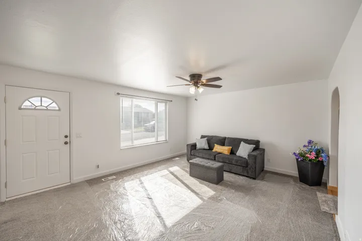 White painted walls, light-toned carpet, ceiling fan, arched doorway, and a window with blinds