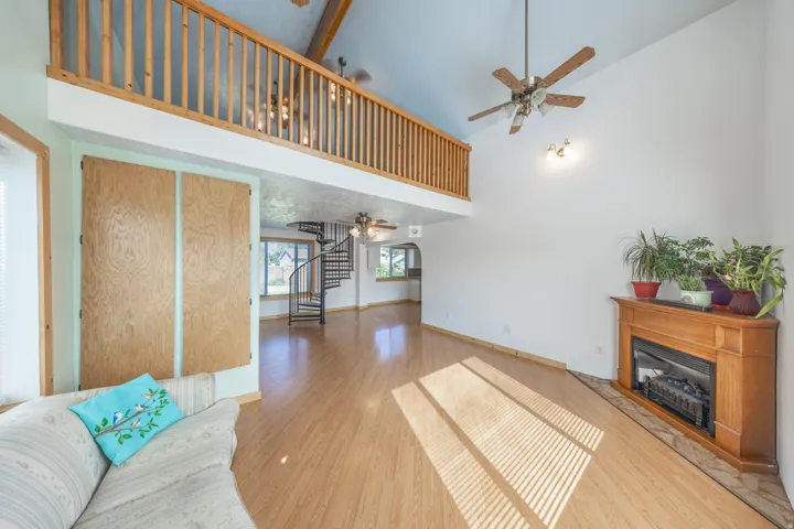 Vaulted ceiling with exposed wood beams, wood-finish flooring, corner fireplace with wood mantel, and a spiral staircase