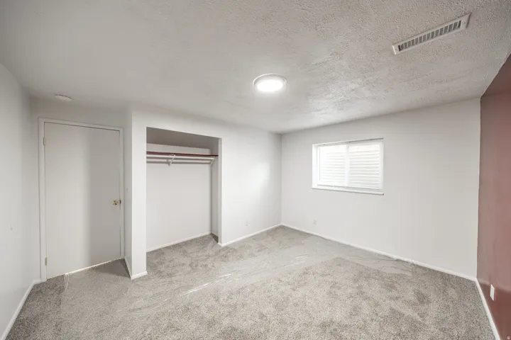 Neutral wall paint with an accent wall, window with blinds, and built-in closet with hanging rod