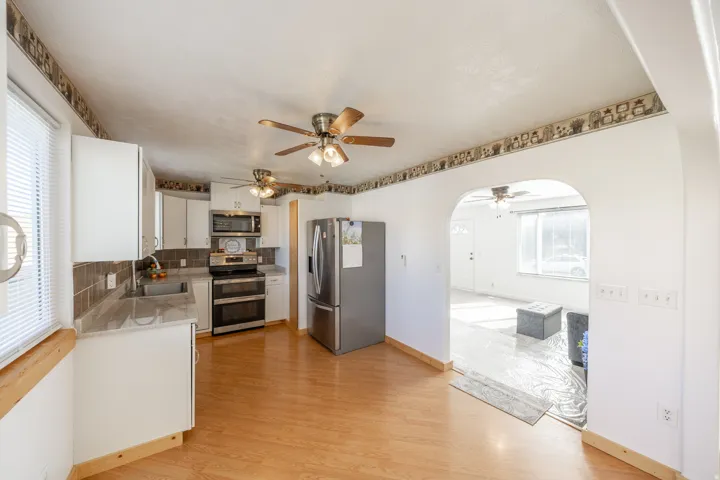 Kitchen featuring wood-finish flooring, stainless steel appliances, white cabinetry, brown tile backsplash, and light-toned countertops