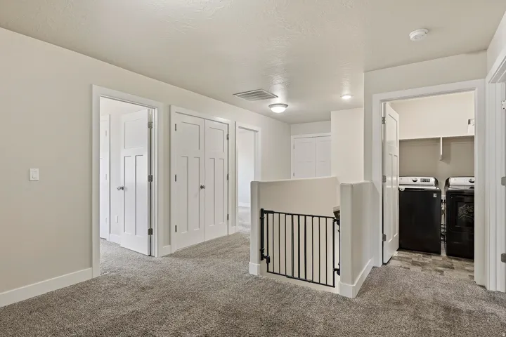 Carpeted hallway with white interior doors, recessed lighting, and a built-in laundry area featuring a tile floor and shelving