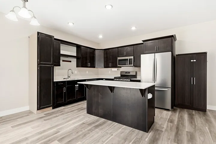 Kitchen featuring dark wood-finish cabinetry, white countertops, stainless steel appliances, a center island, and wood-finish flooring