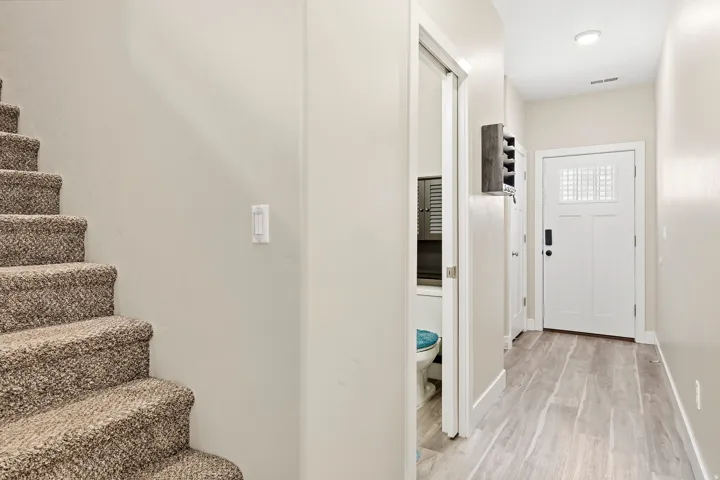 Carpeted staircase, wood-finish flooring, recessed lighting, and a partial view of a bathroom with louvered cabinetry