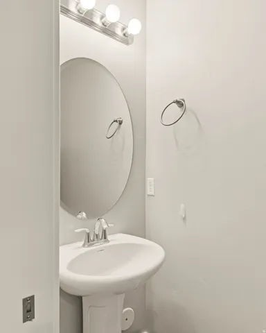 Pedestal sink with chrome faucet, circular mirror, and brushed nickel vanity lighting