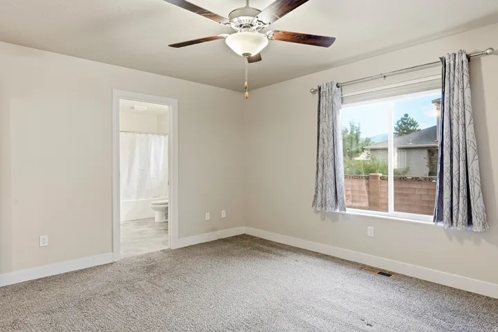 Plush carpeted flooring, a ceiling fan with light fixture, and a window with white trim