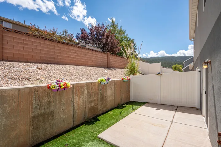 Compact outdoor area featuring a concrete patio, artificial turf, and a white privacy fence