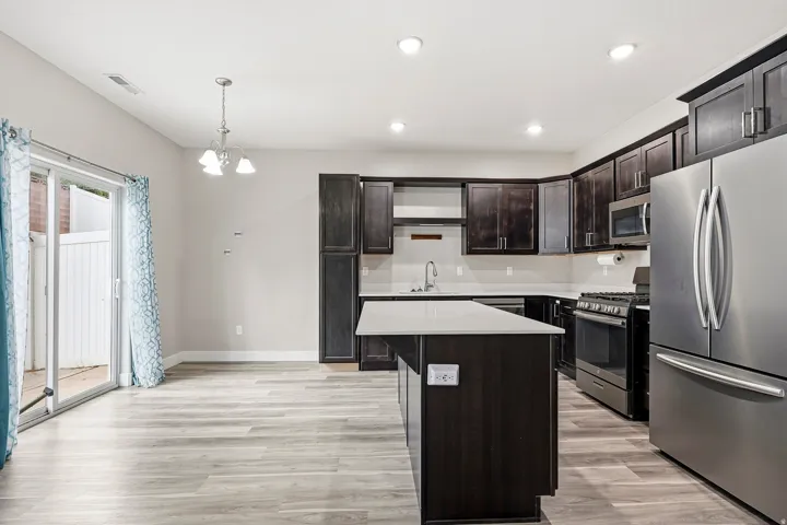 Kitchen featuring dark wood-finish cabinetry, stainless steel appliances, a center island with countertop, and wood-finish flooring