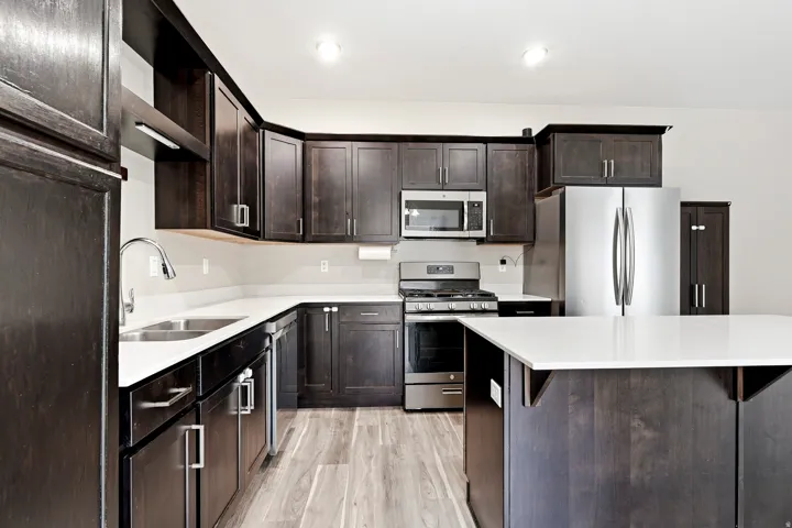 Kitchen featuring dark wood-finish cabinetry, light-toned countertops, stainless steel appliances, a center island, and wood-finish flooring