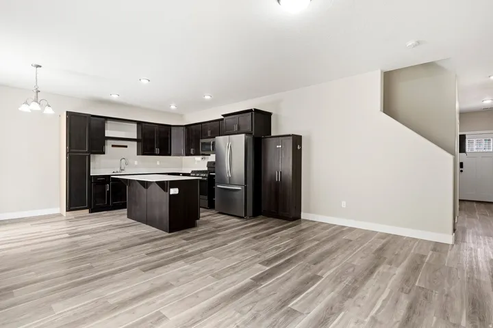 Spacious kitchen with dark wood-finish cabinetry, stainless steel appliances, a center island with a light-toned countertop, and recessed lighting