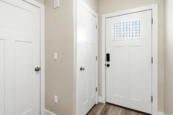 Bright entryway showcasing multiple white six-panel doors with polished hardware, decorative transom window with geometric patterning, and warm neutral walls