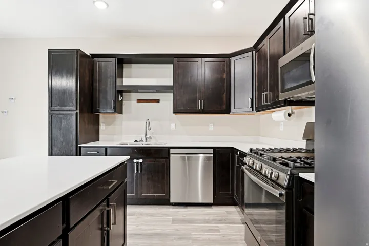 Kitchen featuring dark wood-finish cabinetry, light-toned countertops, stainless steel appliances, and wood-finish flooring
