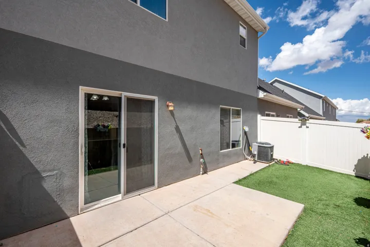 Patio area featuring a sliding glass door, stucco exterior, concrete paving, and a white privacy fence
