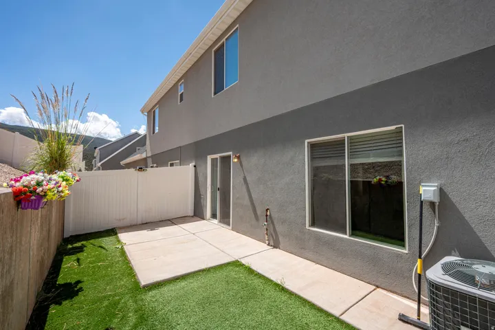 Private rear patio featuring concrete pavers, artificial turf, and a white privacy fence