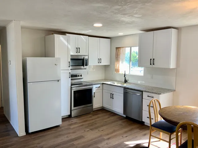 White cabinetry with matte black hardware, stainless steel appliances, granite-style countertops, white subway tile backsplash, and wood-finish flooring