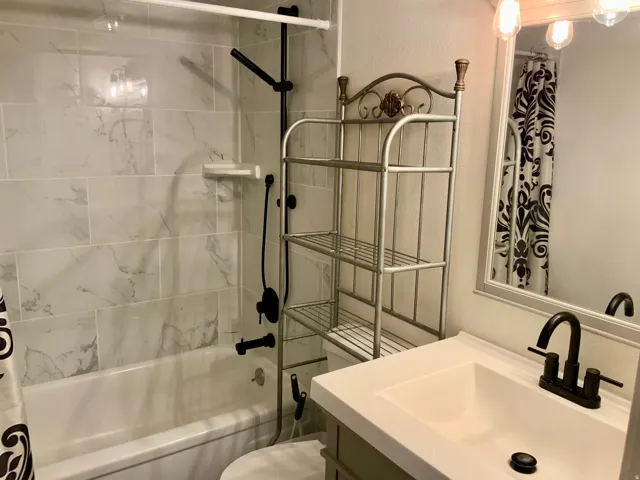 Bathtub with subway tile surround, matte black shower fixtures, vanity with integrated sink, and an illuminated mirror