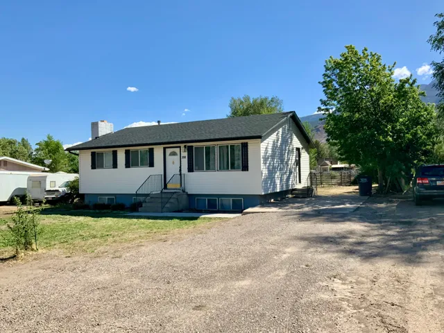 White siding exterior with black shutters, dark shingle roof, and a gravel driveway