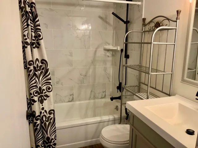 Bathtub with white subway tile surround, single vanity with integrated sink, and wood-finish flooring