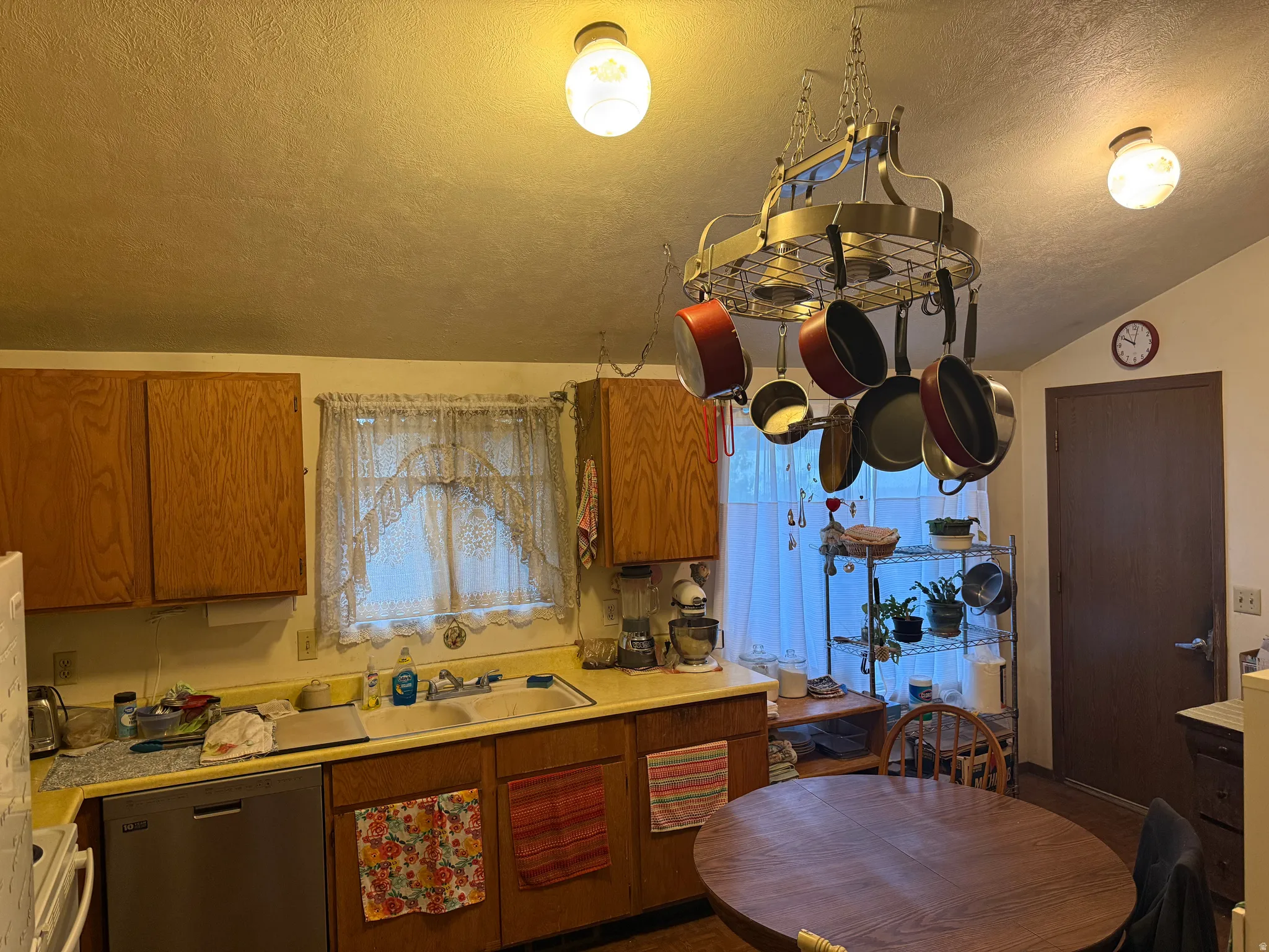 Galley kitchen featuring wood cabinetry, stainless steel dishwasher, double basin sink, and a pot rack