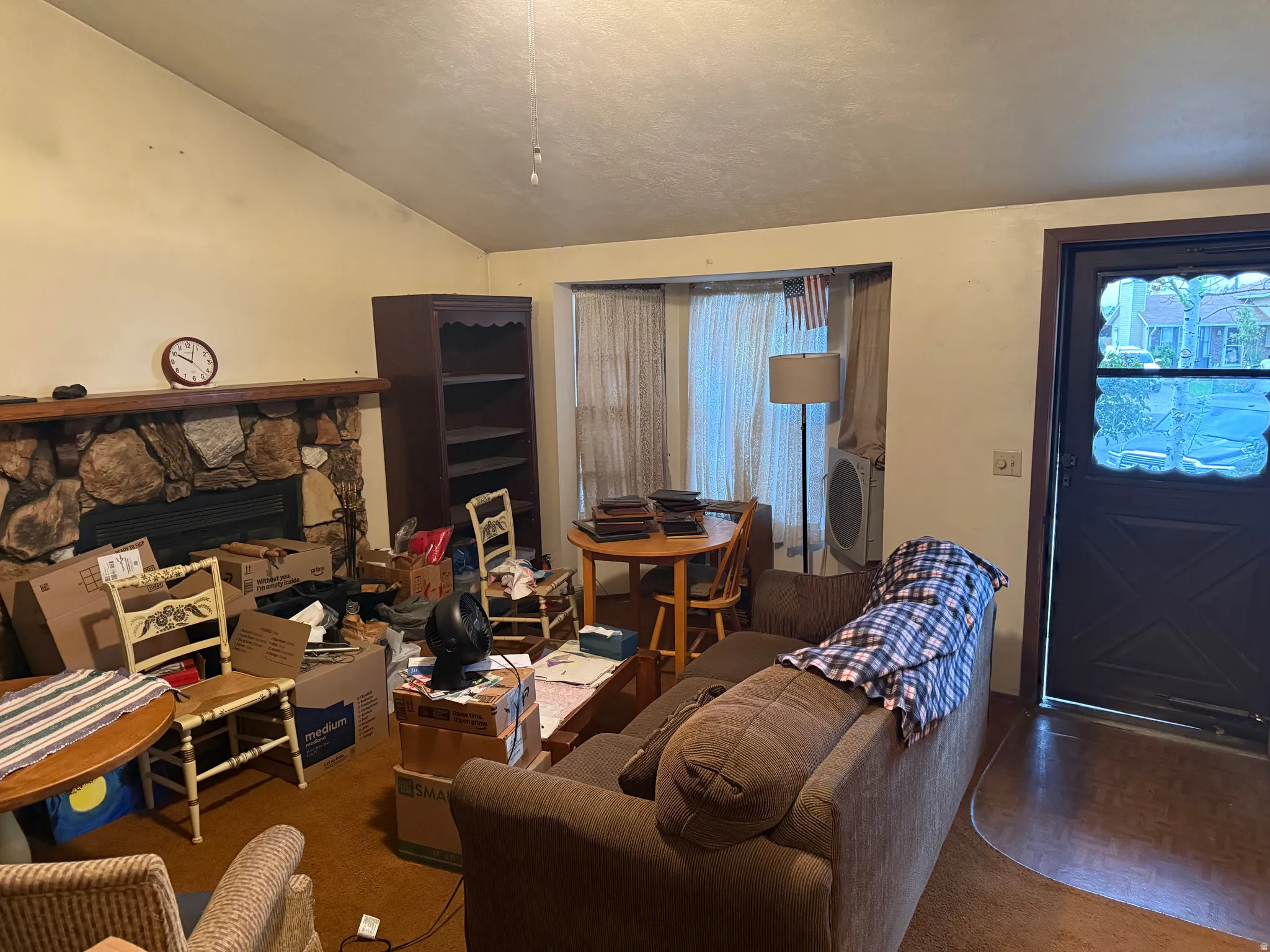 Vaulted ceiling living area featuring a stone-clad fireplace with a wood mantel, a built-in bookshelf, and an entry door with decorative glass