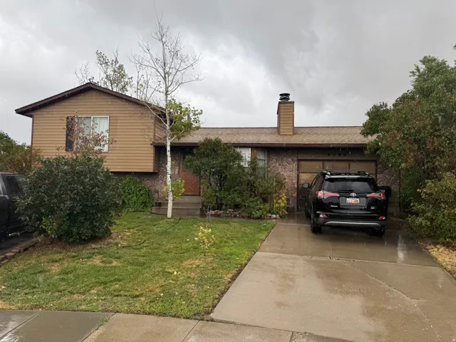 Split-level residence featuring a prominent chimney, an attached garage, and a concrete driveway