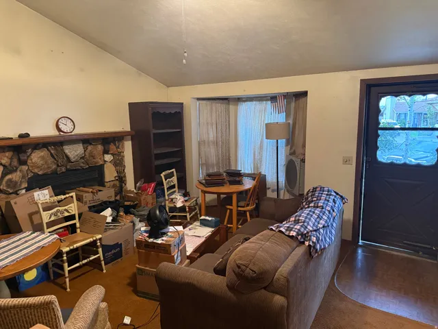 Vaulted ceiling living area featuring a stone-clad fireplace with a wood mantel, a built-in bookshelf, and an entry door with decorative glass