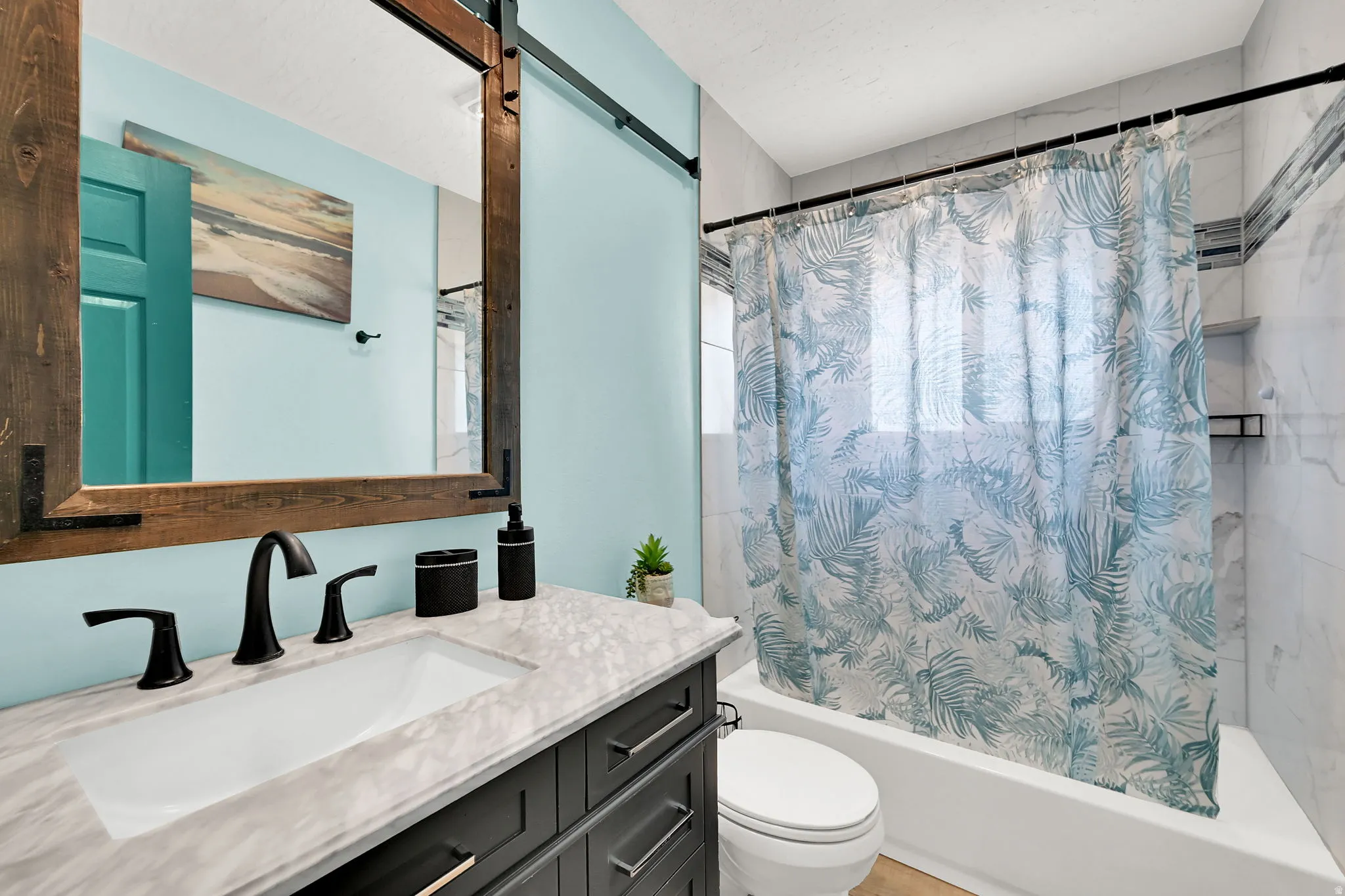 Bathroom featuring a vanity with a rectangular undermount sink, a wood-framed mirror, a built-in bathtub, and tiled walls with an accent strip