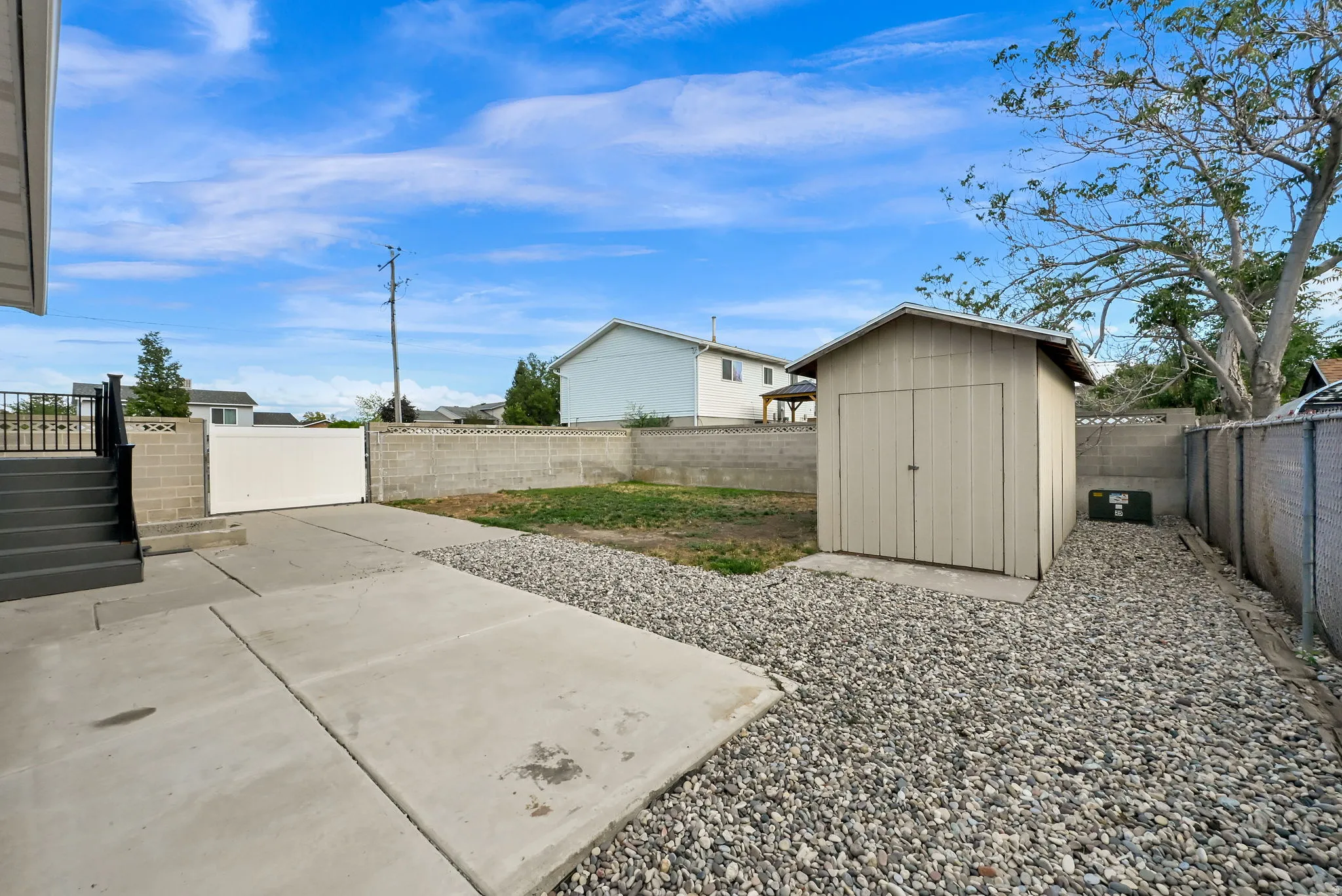 Expansive backyard with a concrete patio, gravel landscaping, and a detached storage shed