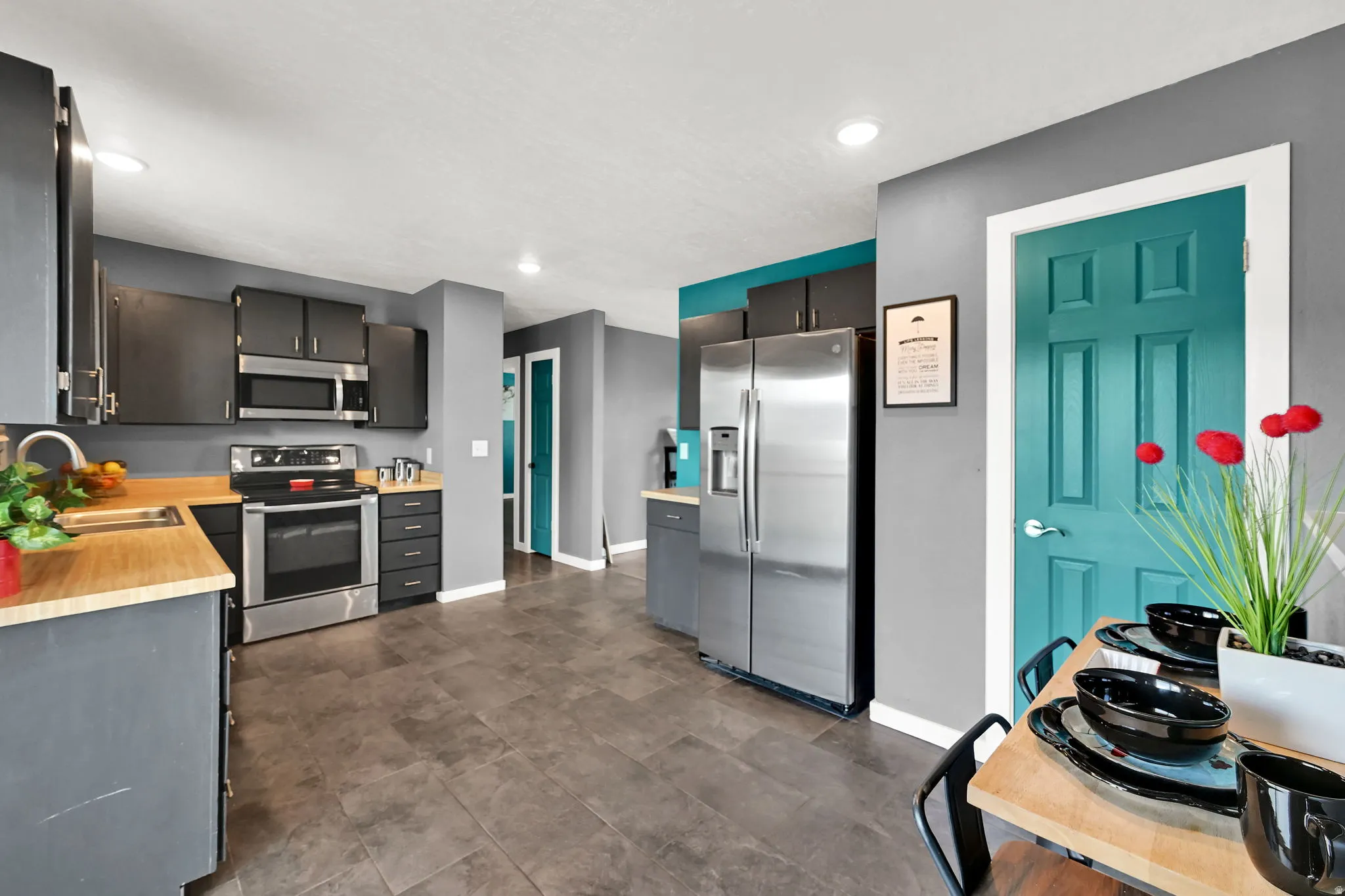 Modern kitchen featuring stainless steel appliances, dark cabinetry, wood-finish countertops, recessed lighting, and tile flooring