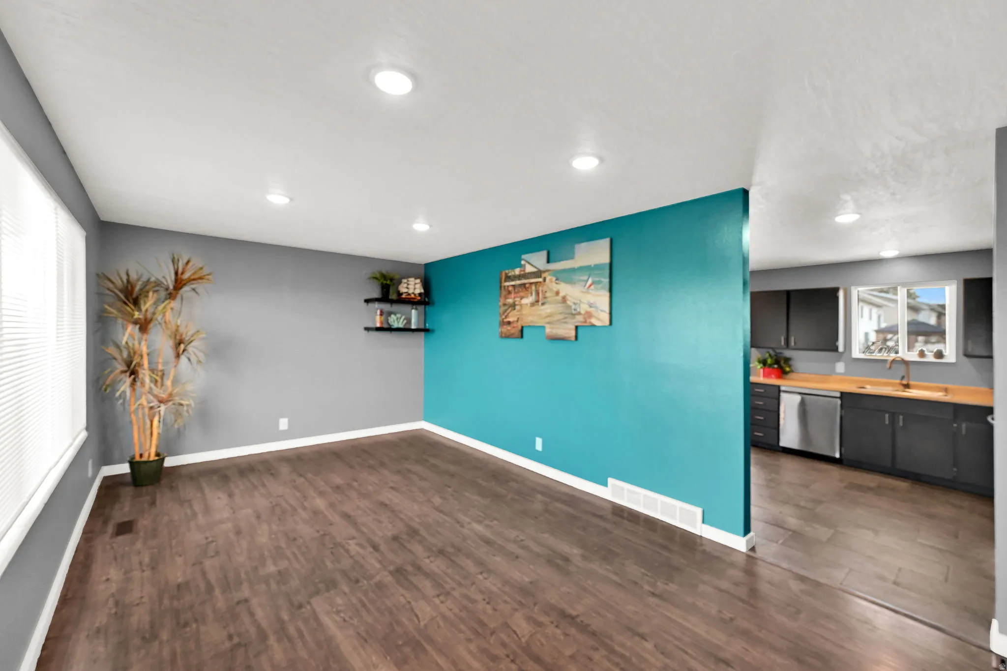 Recessed ceiling lighting, wood-finish flooring, two-tone painted walls, and built-in kitchen cabinetry with a stainless steel dishwasher