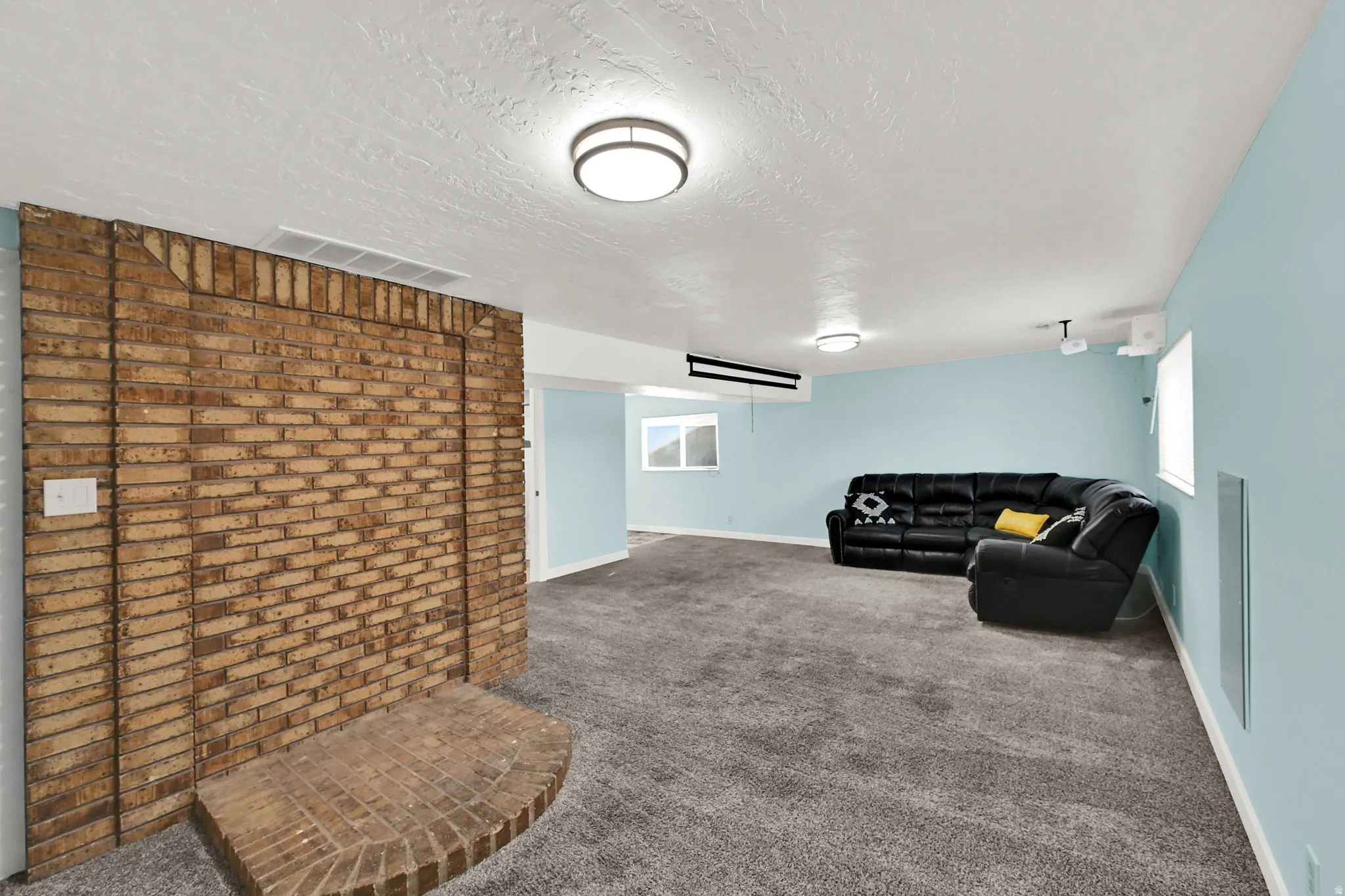 Spacious room featuring a brick fireplace, light blue painted walls, and gray carpeting