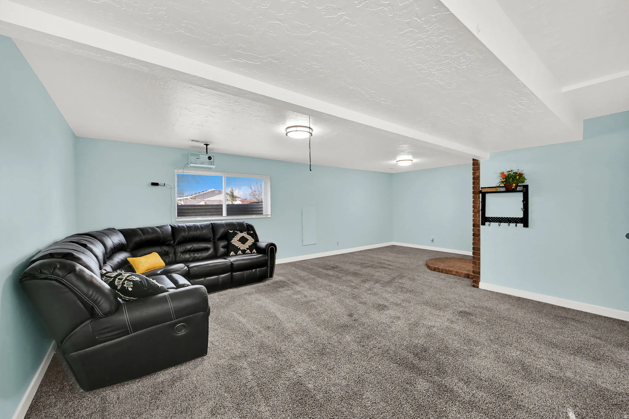 Spacious room featuring light blue walls, gray carpet, and white ceiling beams