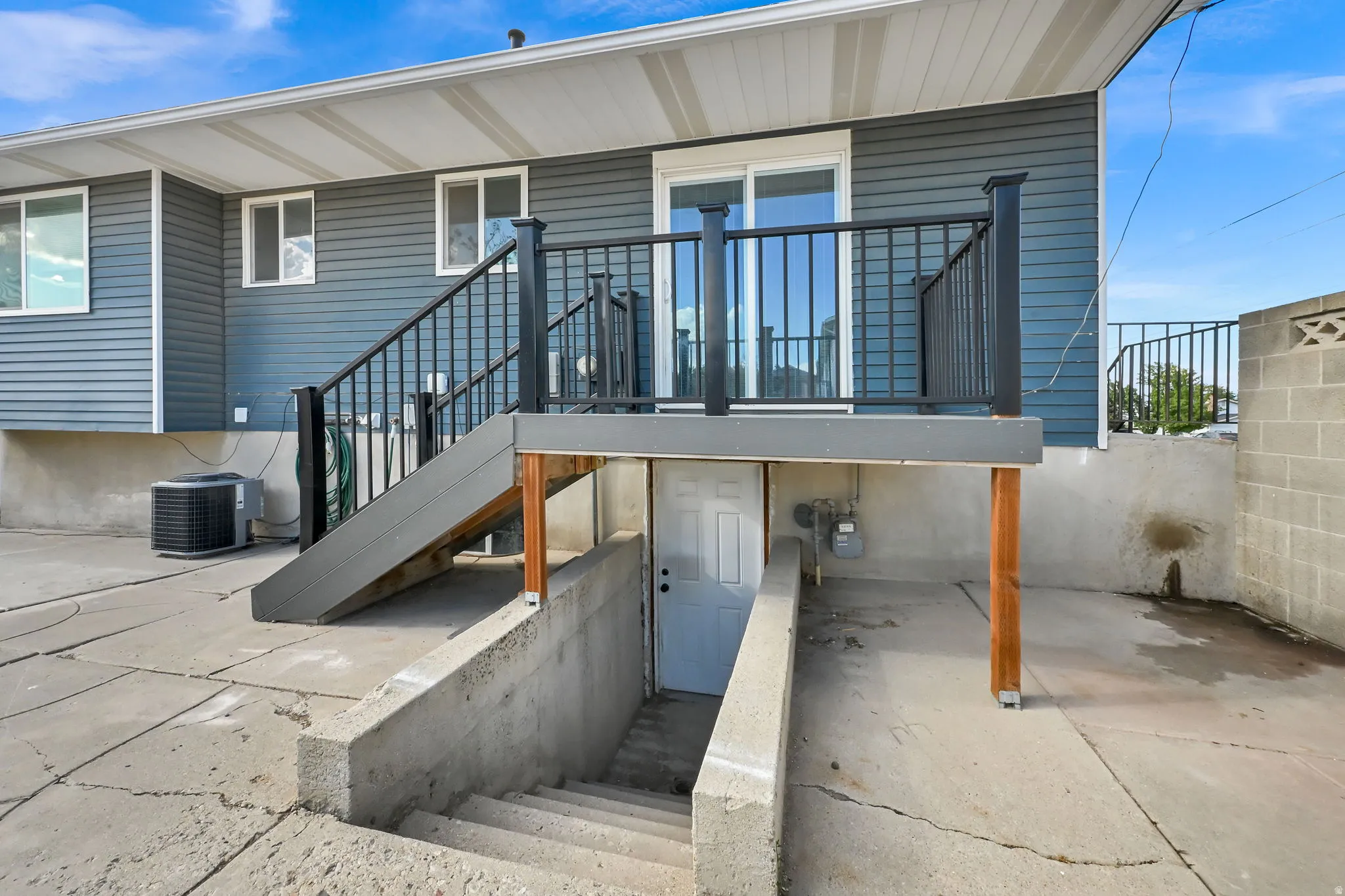 Rear exterior with a concrete patio, a raised deck with dark railings, and a lower-level separate entrance