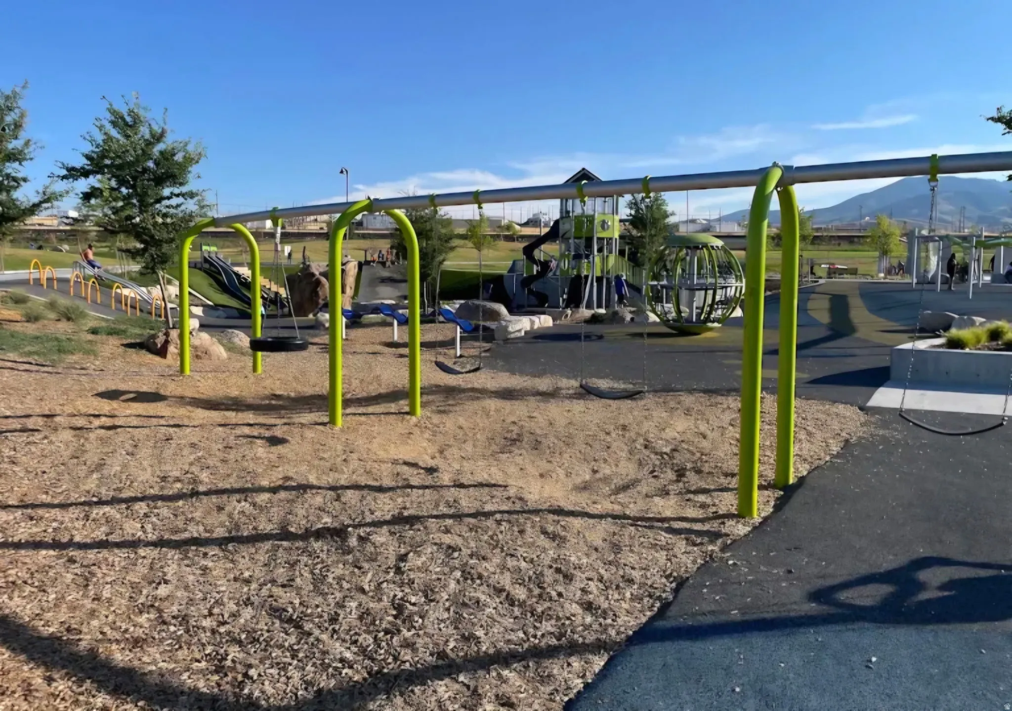 Community playground with multiple swing sets, a slide, climbing structures, and a wood chip ground cover